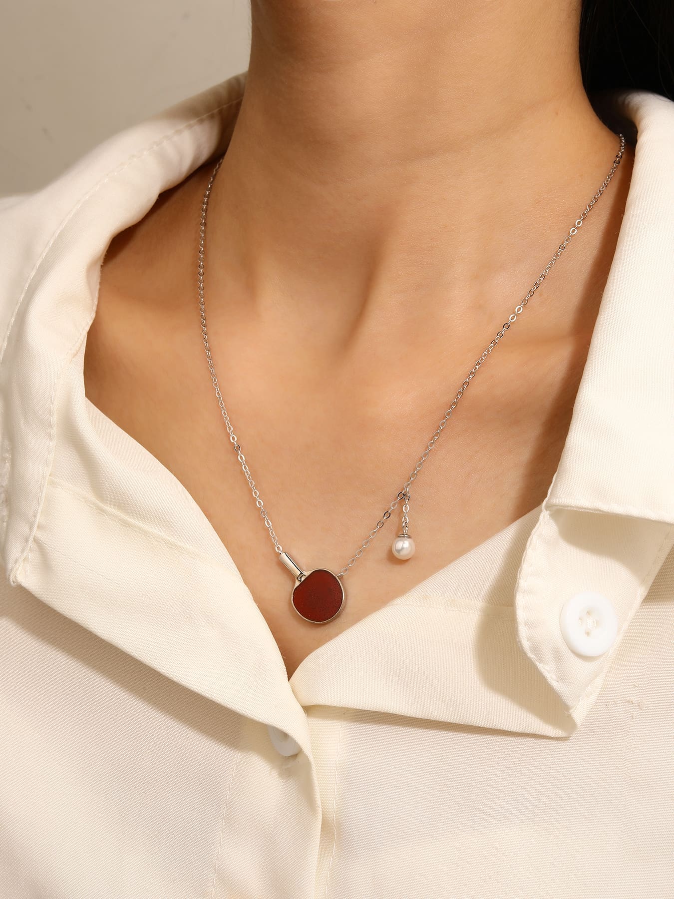 Burgundy enamel table-tennis paddle and pearl ball pendant necklace, crafted with hallmarked, rhodium-plated 925 sterling silver – worn view – DRESCHER Jewellery®